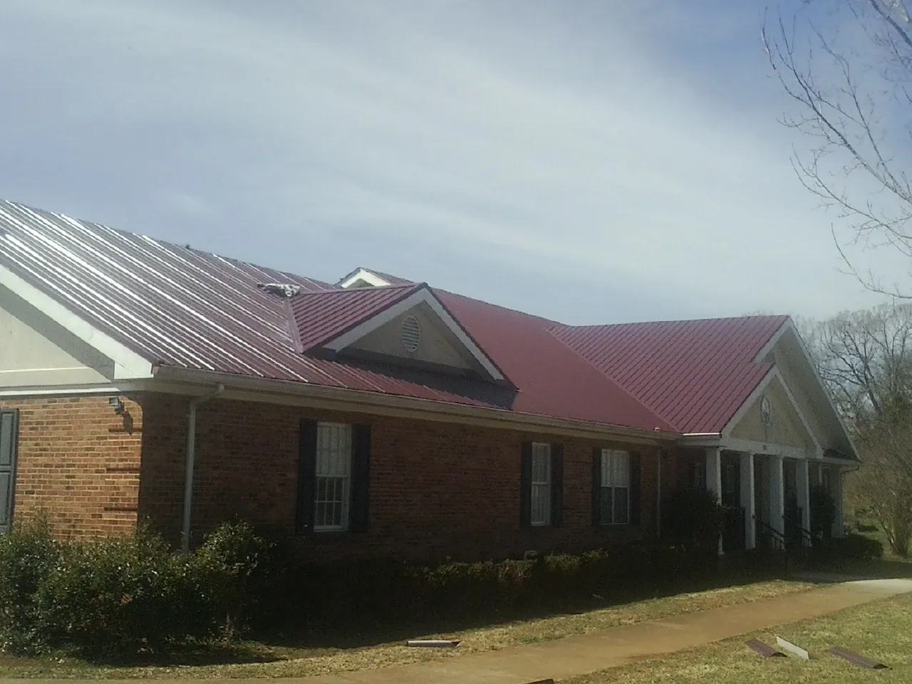 Red metal roof with gabled entries on a long brick building, from a Hail Damage Roof Repair job in Otoe