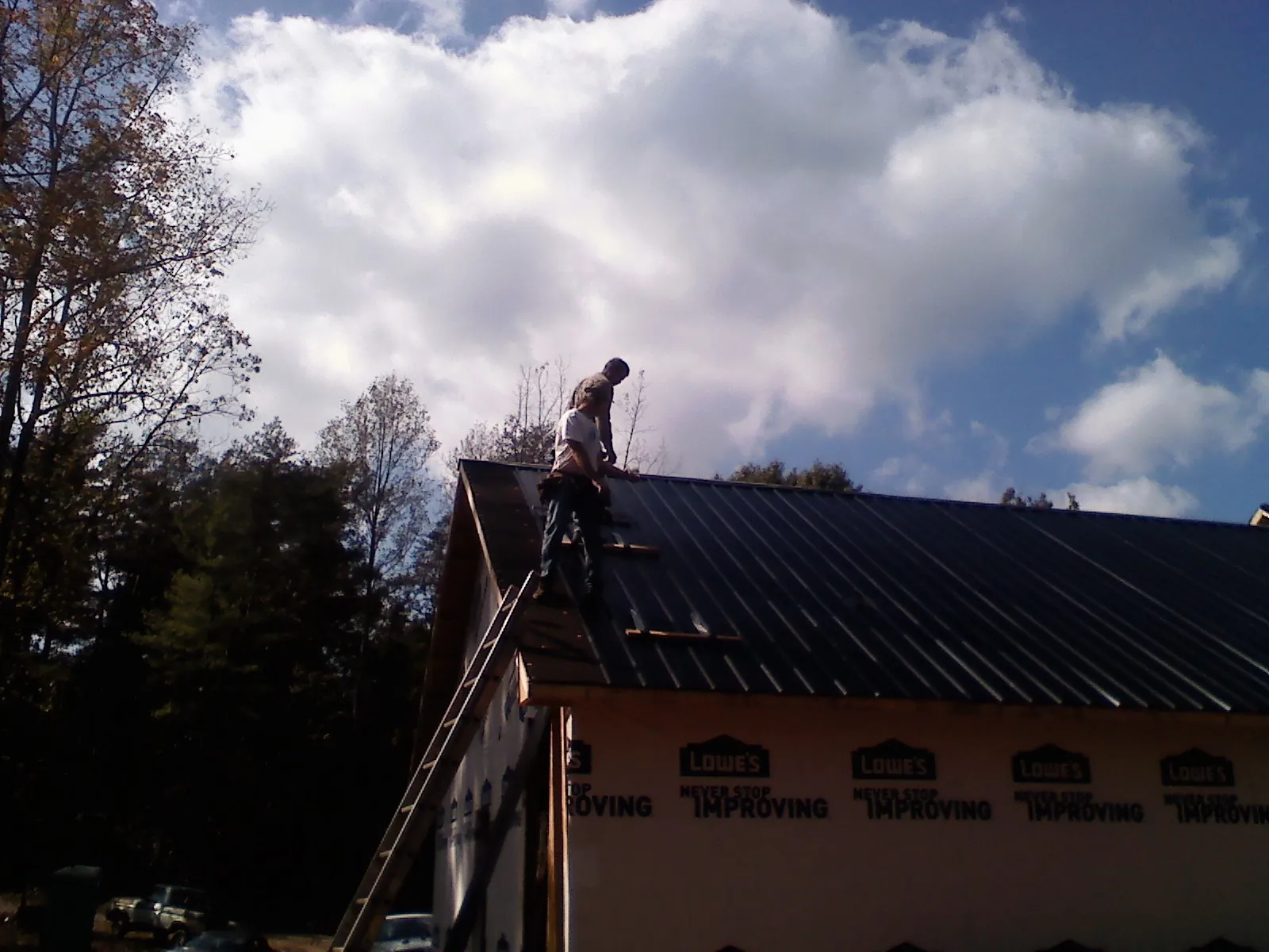 Roofer fastening dark metal panels high against a cloudy sky, from a Roof Inspection job in Otoe